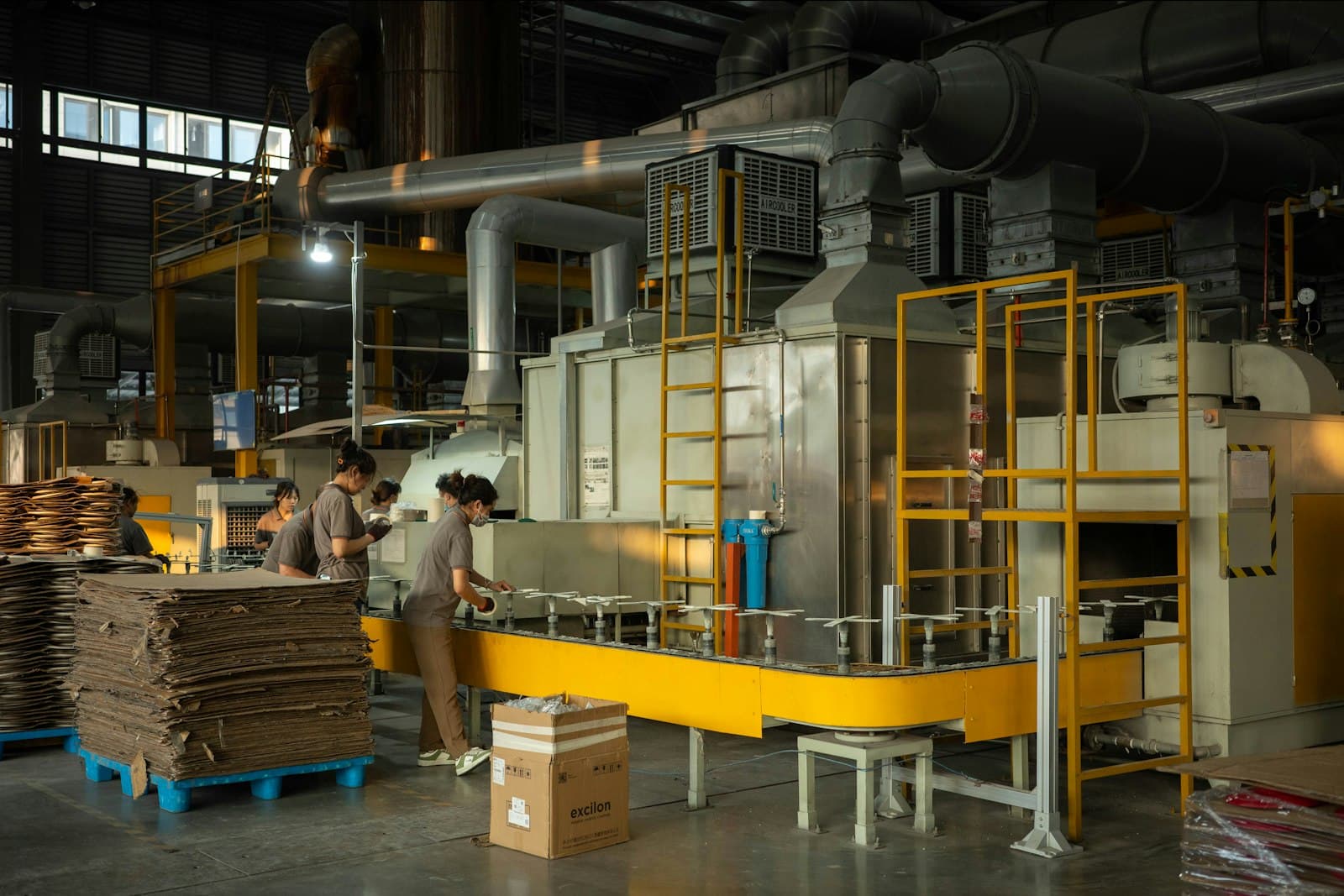 Stacks of corrugated board beside a converting line, with a worker at the machine