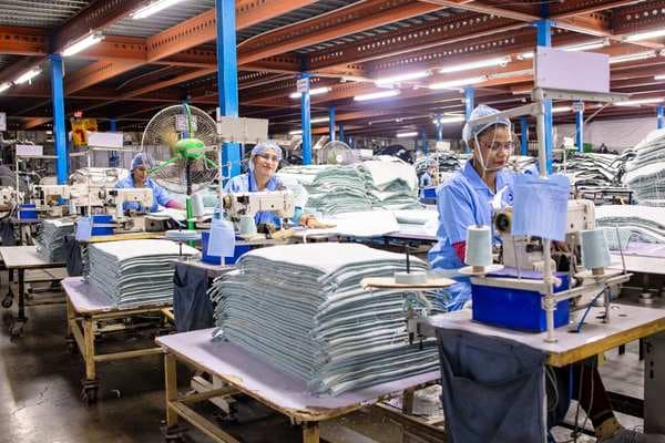 Operators at sewing machines beside stacks of cut fabric panels on a garment production floor